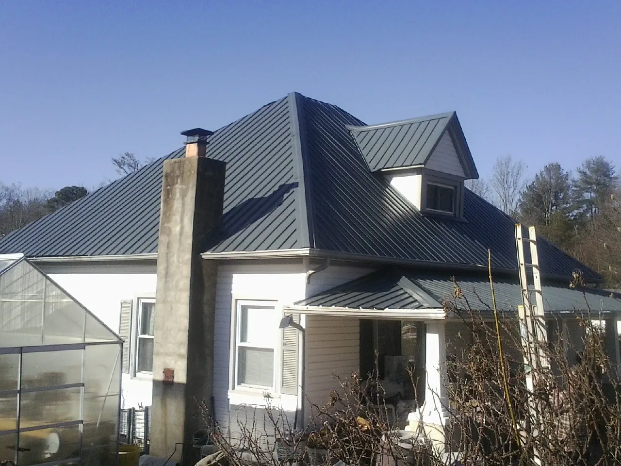 Dark blue standing seam metal roof on a white farmhouse with dormer — Slate & Tile Roof Repair by Roofing Brothers in Ozone Park