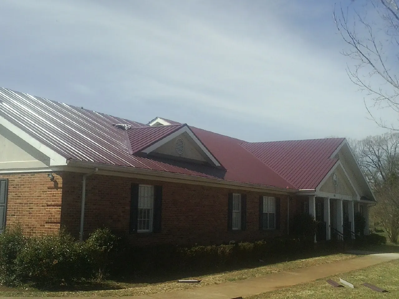 Red metal roof with gabled entries on a long brick building, from a Hail Damage Roof Repair job in Ozone Park