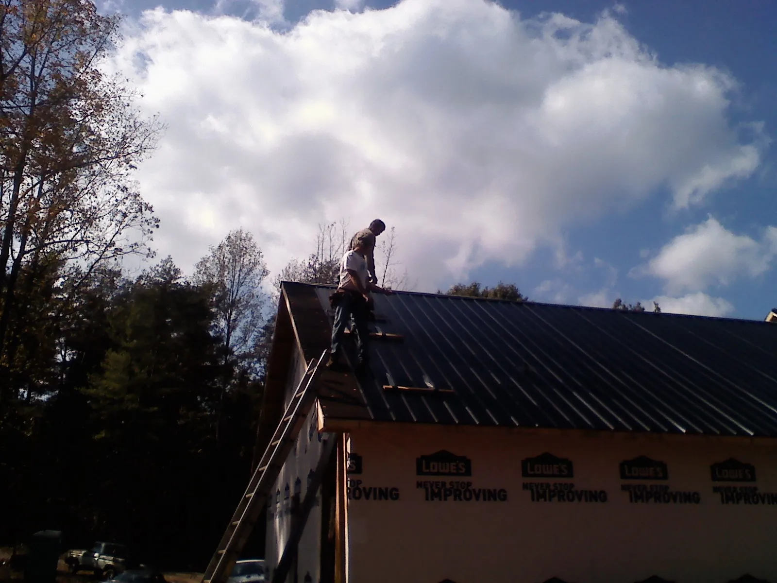 Roofer fastening dark metal panels high against a cloudy sky, from a Roof Inspection job in Ozone Park