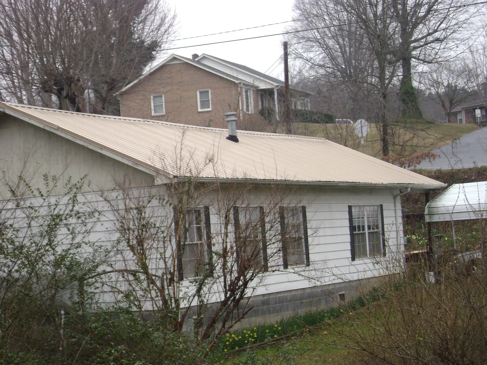 Tan metal roof on a white sided house set into a hillside — Commercial Roofing by Roofing Brothers in Ozone Park