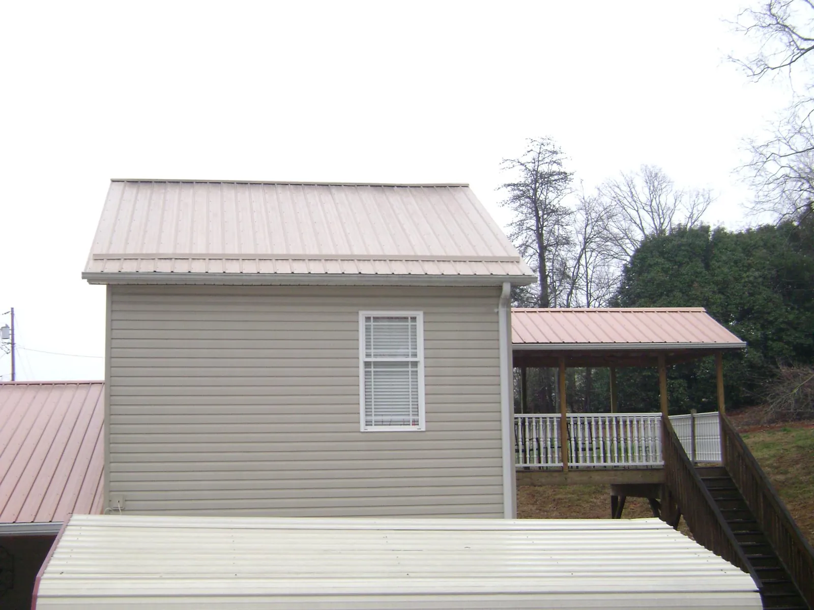 Tan metal roofs on a two story addition and attached porch, from a Roof Replacement job in Ozone Park
